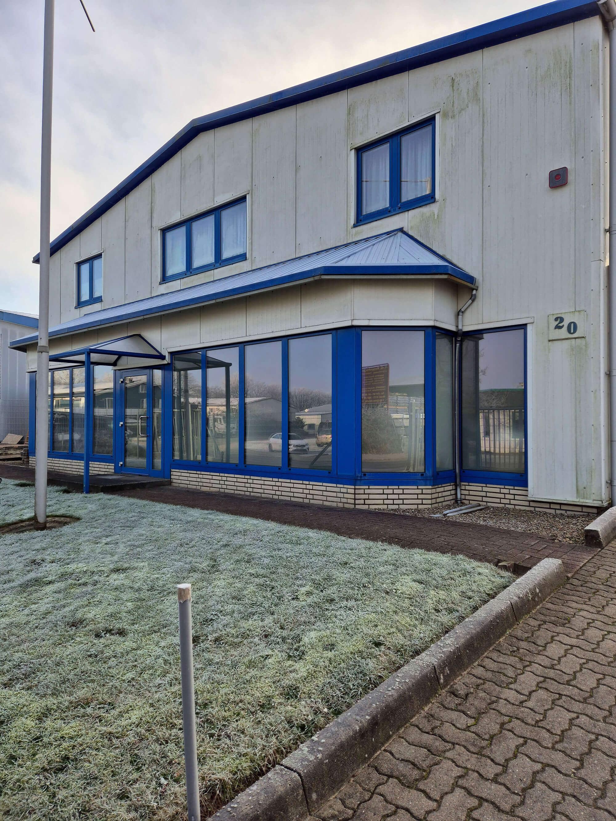 Vorderansicht des Firmengebäude im Winter, Glasfassade mit blauen Rahmen, das Gras im Vordergrund hat Raureif